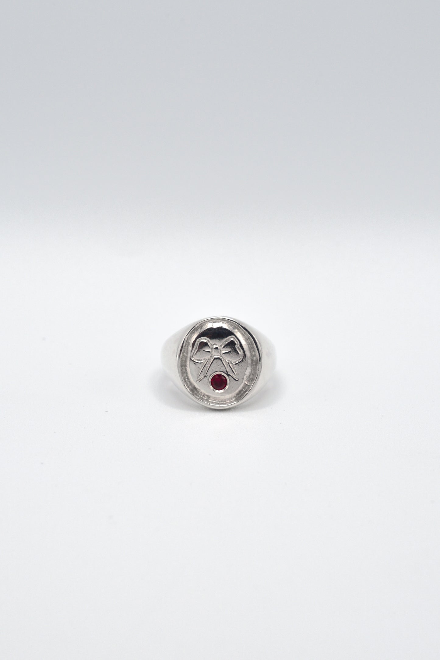 Signet ring with a red gemstone and engraved bow on a white background