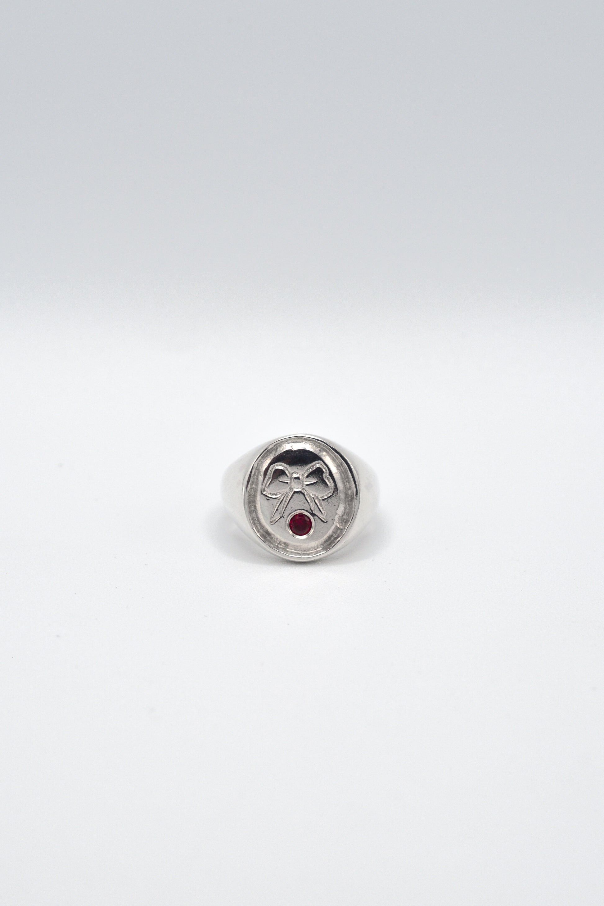 Signet ring with a red gemstone and engraved bow on a white background