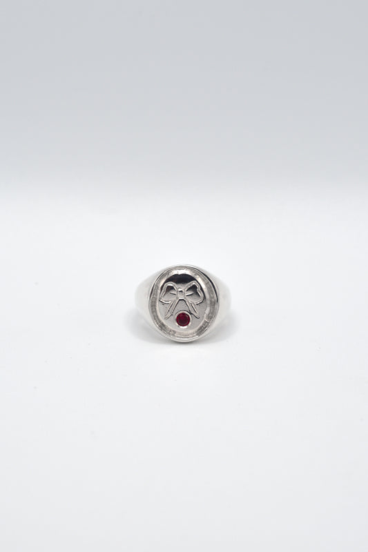 Signet ring with a red gemstone and engraved bow on a white background