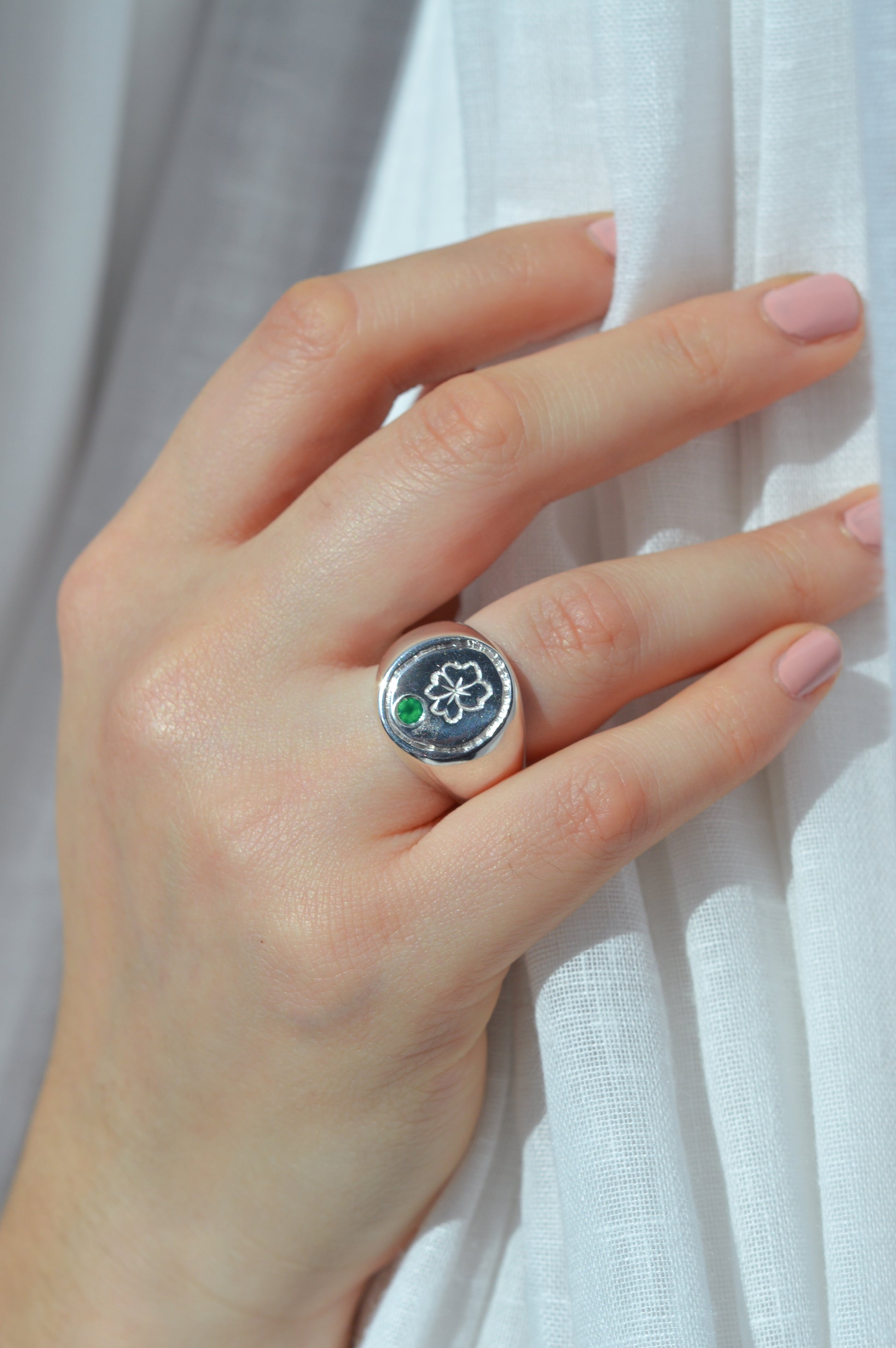 Hand wearing a silver ring with a green stone against a white background