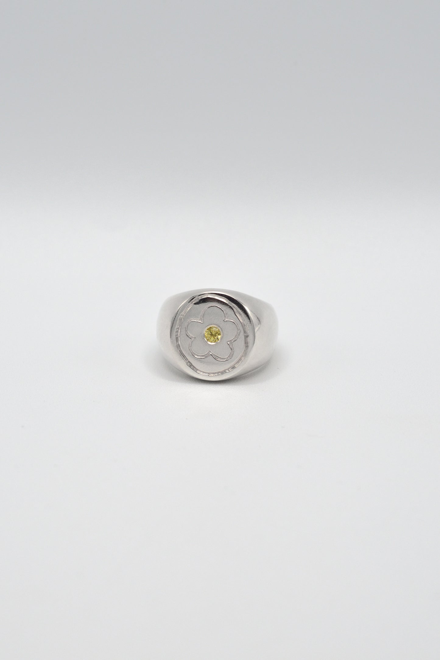 Silver ring with a yellow gemstone on a light gray background