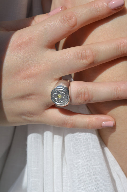 Close-up of a hand wearing a silver ring with a floral design on a light background