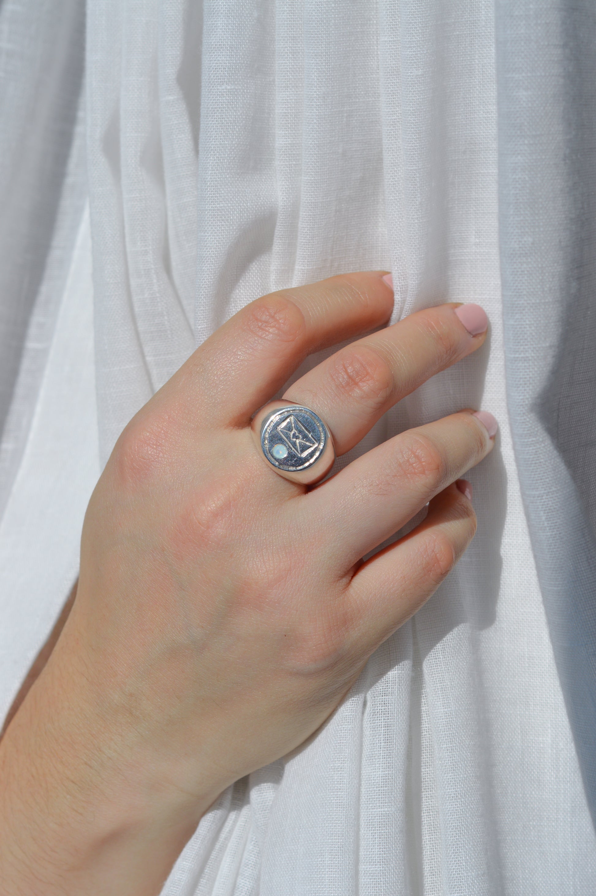 Hand wearing a silver ring with a circular design on a white fabric background